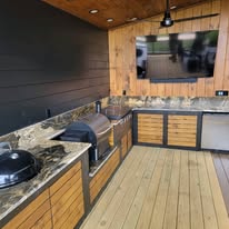 Covered outdoor kitchen with granite counters, grill, and wood cabinetry
